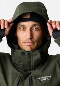 Zielona, wodoodporna kurtka z wysokim kołnierzem i odpinanym kapturem. Posiada naszywkę z logo oraz czarne akcenty na mankietach i wewnętrznej podszewce.