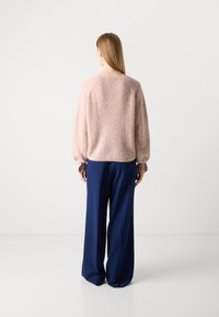 Roze fuzzy trui met raglanmouwen, gecombineerd met een wijde navyblauwe broek. De trui heeft een zachte textuur en een aansluitende zoom.