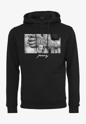 Svart hettegenser med et frontgrafikk av hender med tatoveringer som holder et smykke. Ordet "pray" er trykt i hvit skrift under bildet.