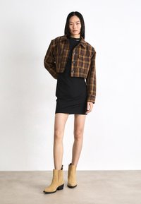 Cropped, plaid jacket in orange and brown, black dress, and beige suede ankle boots with a block heel and decorative stitching.