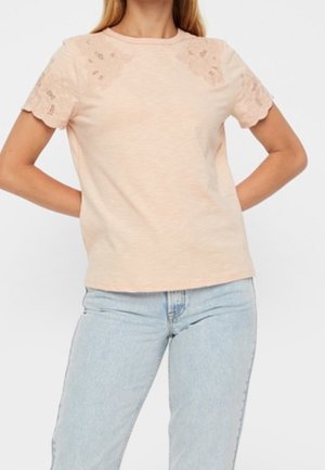 Lichtroze t-shirt met korte scalloped kantmouwen, ronde hals en een gladde textuur. Gepaard met lichtblauwe spijkerbroek.