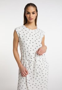 Hvid kjole med korte ærmer, der har et struktureret stof og små sorte blomstermønstre, snøret ind i taljen med et matchende bånd.