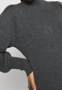 Pull gris côtelé à col haut, avec des épaules bouffantes et des manches longues ajustées. Texture douce avec un léger éclat.