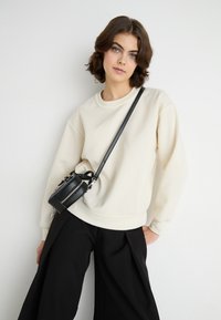 Kremfarget sweatshirt med rund hals, lange ermer og ribbet nederkant, sammen med høytlivde svarte vide bukser og en liten svart crossover-veske.