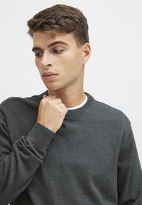 Suéter de cuello redondo en gris oscuro, hecho de un material de punto suave, con puños y dobladillo de canalé. El modelo toca el cuello, con un diseño liso y minimalista.