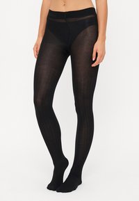 Schwarze Strumpfhosen mit transparenter Optik, die vertikale Rippungen aufweisen. Der Bund ist breit und der Stoff hat eine glatte, leicht glänzende Textur.