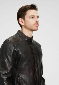 Braune Lederjacke mit Stehkragen, ausgestattet mit einem Frontreißverschluss und Seitentaschen. Das Material hat eine leicht glänzende Oberfläche.