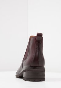 Burgundy nahkasaappaat, joissa on joustavat sivupaneelit, pyöreä kärki, vetotappi ja karhea musta kumipohja. Yksinkertainen muotoilu ja sileä pinta.