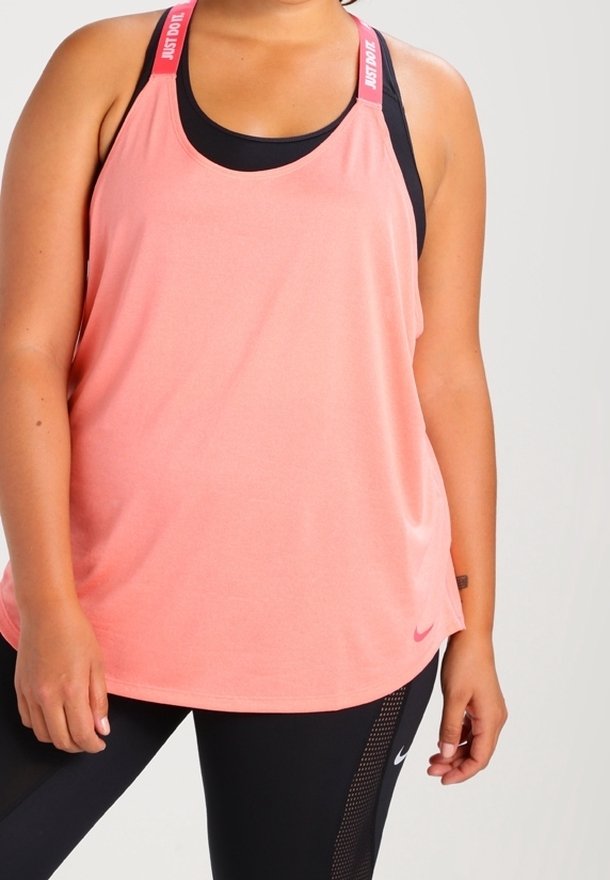 Femme portant un débardeur rose ample avec des bretelles "Just Do It" sur un soutien-gorge de sport noir et des leggings noirs avec des panneaux en mesh.