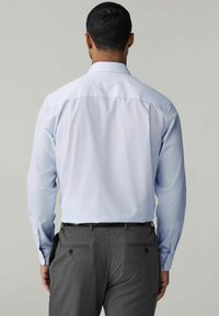 Cămașă de dress rayată albastru deschis, cu mâneci lungi, cu manșete îndoite și guler structurat. Asortată cu pantaloni de dressing gri, cu buzunare.
