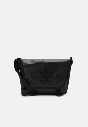 Černá taška přes rameno vyrobená z odolného materiálu, s klopou, nastavitelným popruhem a vystouplým logem Adidas na přední straně.