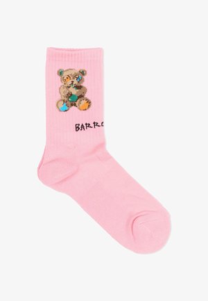 Roze sok met een gepixelde teddybeer met blauwe en oranje vlekken en gedeeltelijk zichtbare zwarte tekst nabij de enkel.