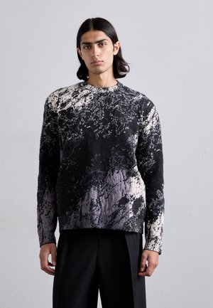 Pulover tricotat cu un model texturat, abstract în alb și negru. Are guler rotund și mâneci lungi, cu o croială lejeră.