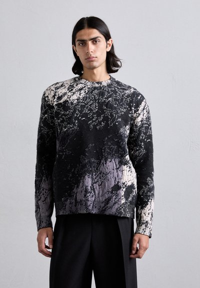 Pull en tricot avec un motif texturé abstrait noir et blanc. Doté d'un col rond et de manches longues, il présente une coupe ample.