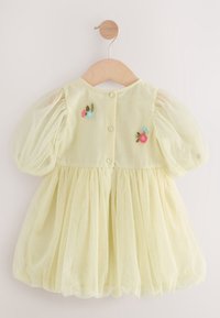 Robe de bébé jaune pâle avec manches bouffantes en voile, jupe froncée, fermeture boutonnée au dos et petites fleurs roses et bleues brodées.