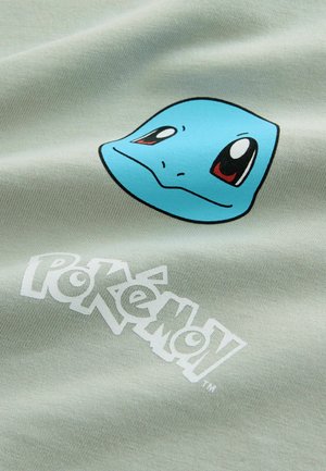 Hellgrüner Stoff mit einem blauen Squirtle-Motiv, roten Augen und schwarzen Umrandungen, begleitet von einem weißen "Pokémon"-Logo darunter.