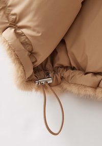 Innenausstattung der tanfarbenen Steppjacke mit weichem Kunstfellfutter. Verfügt über einen metallischen Zugverschluss zum Festziehen und einen elastischen Saum mit Kordelzug.