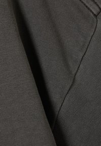 Tummanharmaa puuvillakangas, jossa on sileä pinta ja hienostunut ribbineuloskuvio, ja taitettu osa, joka paljastaa ompelun yksityiskohdat.