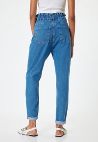 Jeans de mezclilla azul con un cinturón elástico fruncido, diseño de cinco bolsillos y puños enrollados en los tobillos, con un acabado texturizado.
