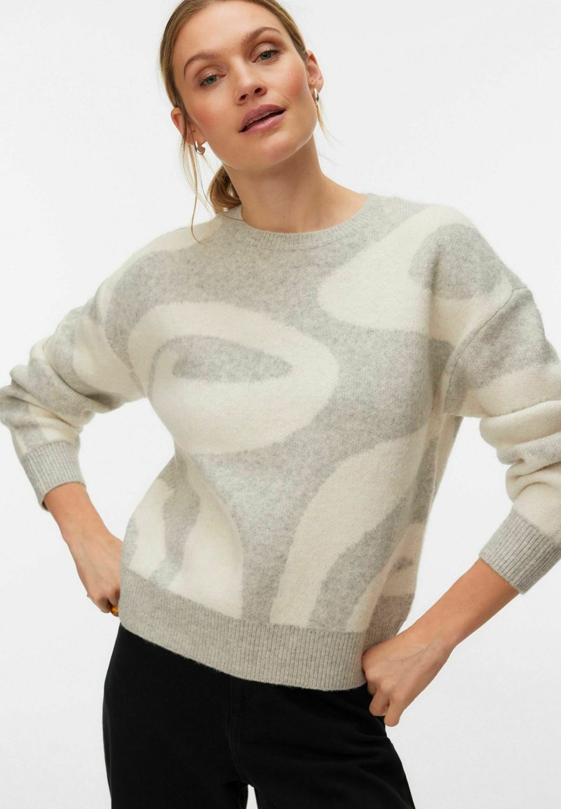 Pull gris clair tricoté avec motifs abstraits crème, col rond et poignets côtelés. Texture douce, coupe décontractée et design légèrement surdimensionné.