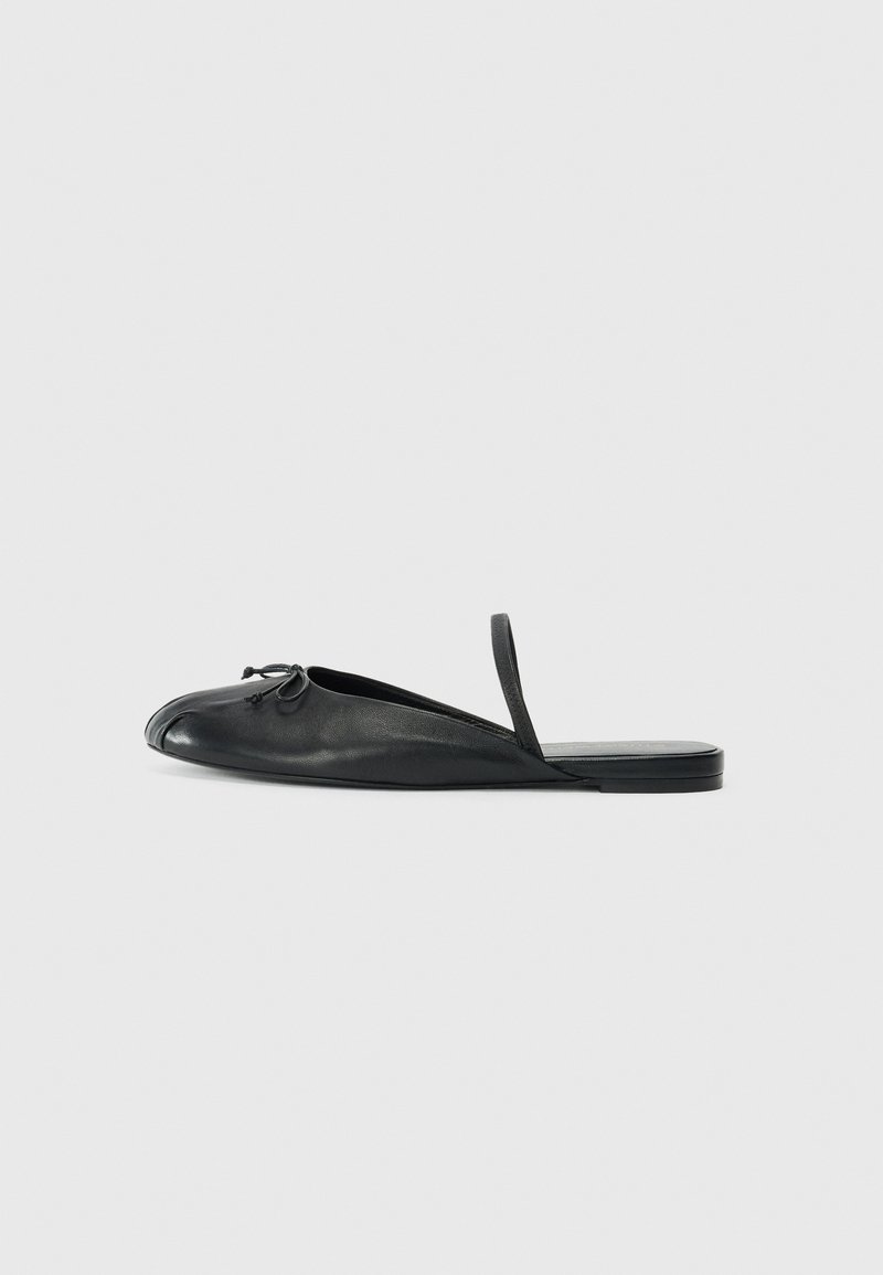 Black leather slip-on shoe featuring a rounded toe, side cutouts, and a thin strap at the heel. Smooth texture with a minimalistic design.