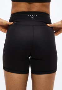 Άτομο που φοράει μαύρα αθλητικά σορτς Puma HYROX με ψηλή μέση, τραβώντας ελαφρώς την ζώνη με τα δύο χέρια.