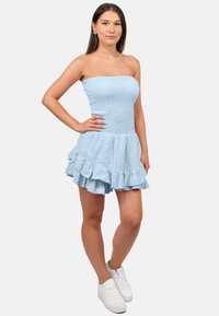 Robe sans bretelles bleu clair avec un tissu texturé, ourlet volanté et corsage ajusté, associée à des baskets blanches.