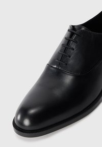 Chaussure de soirée en cuir noir poli avec un laçage fermé et un bout arrondi, présentée en gros plan angulaire sur un fond blanc.