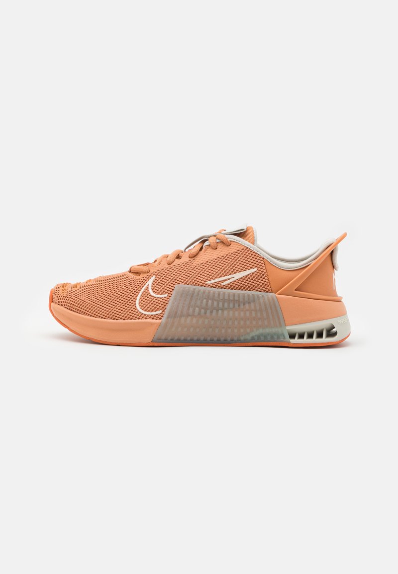 Nike sporta apavi gaiši oranžā sietā ar teksturētu pelēku paneļa, gumijas zoli un noapaļotu pirksta dizainu.
