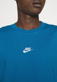 Modrá bavlněná trika s kulatým výstřihem a vyšitým bílým logem Nike na prsou. Látka má hladký povrch.