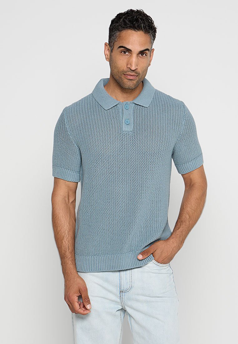Hellblaues Polohemd mit kurzen Ärmeln, strukturiertem Strickmuster, zweifach knöpfbarer Blende sowie geripptem Kragen und Saum, kombiniert mit hellen Jeans aus Denim.