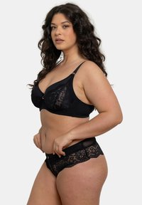 Bralette en dentelle noire avec un design à coussinets doux, dotée de bretelles réglables et d'un bord en dentelle découpé. Culottes en dentelle noire assorties visibles en dessous.