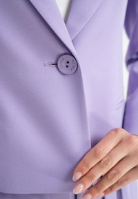 Jasnofioletowa marynarka z pojedynczym zapięciem na guzik z napisem "CLICK". Miękka tekstura materiału i dopasowany krój z klapami.