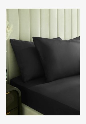 Schwarze Kissenbezüge und Spannbettlaken auf einem Bett mit einem hellgrünen gepolsterten Kopfteil und einem dunkelgrünen Nachttisch.