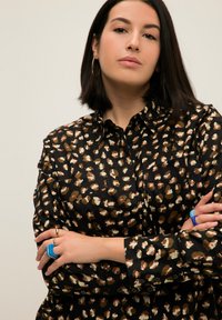 Camicia nera con bottoni caratterizzata da un motivo di forme astratte in crema, marrone e verde. Maniche lunghe con polsini a bottone e colletto.