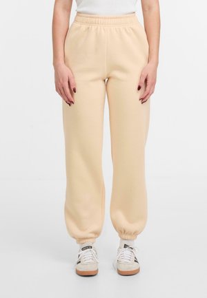 Helle beige Sweatpants mit elastischem Bund und gerippten Bündchen, aus einem weichen Material gefertigt. Kombiniert mit weißen und beigen Sneakers.
