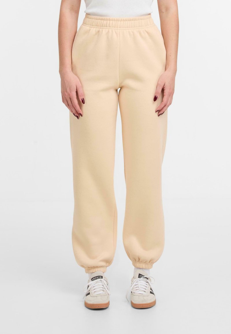 Helle beige Sweatpants mit elastischem Bund und gerippten Bündchen, aus einem weichen Material gefertigt. Kombiniert mit weißen und beigen Sneakers.