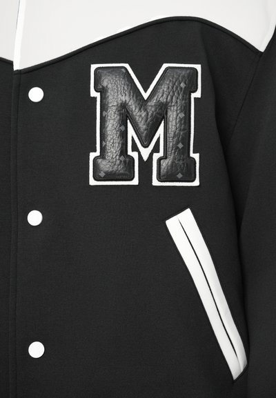 Čierna univerzitná bunda s textúrovanou koženou ná�šivkou "M" v čiernej farbe, bielymi akcentmi a bočným vreckom s výrazným bielym pruhom.