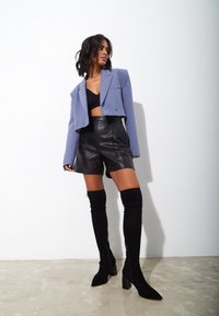 Geknipt lavendelkleurig blazer, zwarte leren shorts en zwart boven de knie reikende laarzen. Gladde texturen en een getailleerd ontwerp met scherpe vormen.