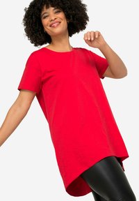 T-shirt rossa a maniche corte realizzata in un tessuto morbido e leggero, con vestibilità rilassata e orlo arrotondato, abbinata a leggings neri.