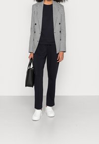 Černobílý kostkovaný dvojřadý blejzr přes námořnický top, spárovaný s námořnickými kalhotami a bílými teniskami, držící černou kabelku.