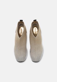 Stivaletti in maglia oro e argento con una vestibilità simile a quella di un calzino, inserti laterali elastici e suole in gomma bianca. Sottopiedi metallici visibili.