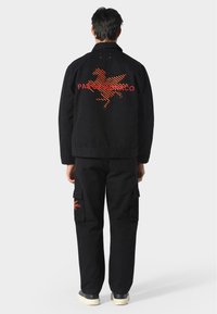 Schwarzes Cargo-Jacke und Hose-Set mit rotem "PAS DE MONACO"-Text und Grafik, im lässigen Schnitt und sichtbaren Taschen an der Hose.