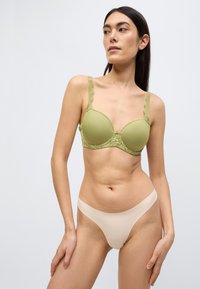 Ελιάς πράσινο επενδεδυμένο σουτιέν με λεπτομέρειες από δαντέλα και ιμάντες με κυματιστό τελείωμα, σετ με γυμνό απαλή αόρατη στρινγκ. Λείο ύφασμα, μοντέρνος σχεδιασμός.