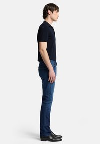 Polo shirt a maniche corte di colore navy abbinato a jeans blu slim fit e stivali neri alla caviglia, che mostrano una silhouette slanciata.