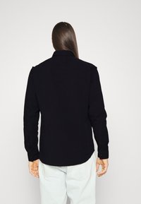 Camisa de algodón negra de botonadura con cuello, mangas largas y dobladillo curvado, con puños de botón y un diseño de color sólido.