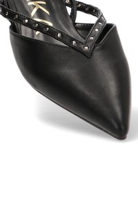 Zapato de salón de cuero negro con punta puntiaguda y correas decorativas con tachuelas. Textura lisa con un diseño elegante que resalta la silueta afilada del zapato.