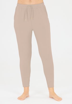 Beige, aangesloten joggers van zacht stof. Voorzien van een elastische tailleband met een trekkoord en zijzakken. Een gladde textuur overal.