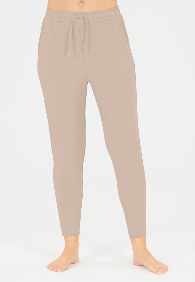 Beige, aangesloten joggers van zacht stof. Voorzien van een elastische tailleband met een trekkoord en zijzakken. Een gladde textuur overal.