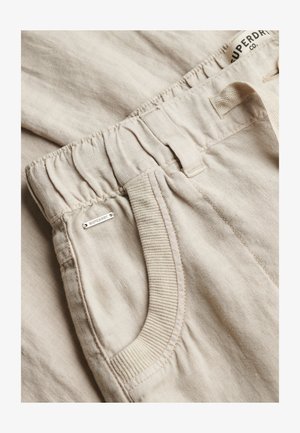 Beige linnen broek met elastische tailleband, geribbelde zakafwerking, broekriemlussen en een klein metalen Superdry-logolabel bij de zak.
